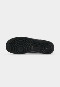Sort gummisål med cirkulære og lineære slidmønstre og en synlig Nike-logo i midten.