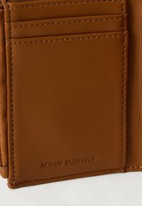 Pruun nahast rahakott, millel on kaardipesad ja reljeefne "ARMANI EXCHANGE" logo allservas.