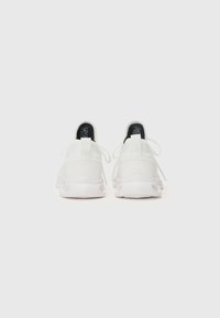 Zapatilla blanca con parte superior texturizada, tacón redondeado, cordones finos y suela ligera con cortes circulares para favorecer la transpirabilidad.