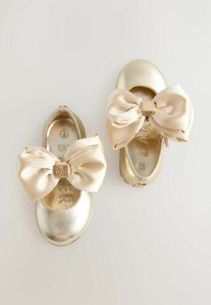 Złote baleriny dla niemowląt z dużymi satynowymi kokardkami, zaokrąglonymi palcami, gładkim metalicznym wykończeniem oraz logo na wnętrzu, które prezentują prosty, elegancki design.