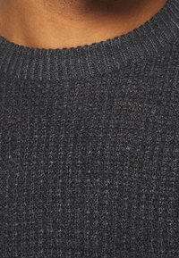 Mörkgrått stickat tröja med en texturerad yta, med en ribbad rund halsringning och subtila tonala variationer i tyget.