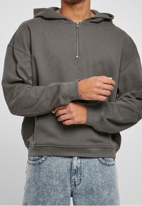 Felpa grigia con cappuccio e mezza zip, morbida al tatto e con polsini a coste. Abbinata a jeans blu scoloriti, che mettono in risalto un look casual.