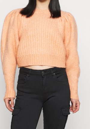 Pull en maille tricotée couleur pêche, avec des manches ballons, un ourlet côtelé épais et un tissu texturé ; associé à un pantalon cargo noir.