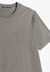Grå kortærmet T-shirt lavet af blødt stof med rund hals og en lomme på venstre bryst, der har ren syning og en afslappet pasform.