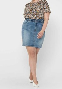 Top a maniche corte floreale con fiori multicolori su uno sfondo scuro, abbinato a una gonna a tubino in denim azzurro chiaro con vita arricciata.