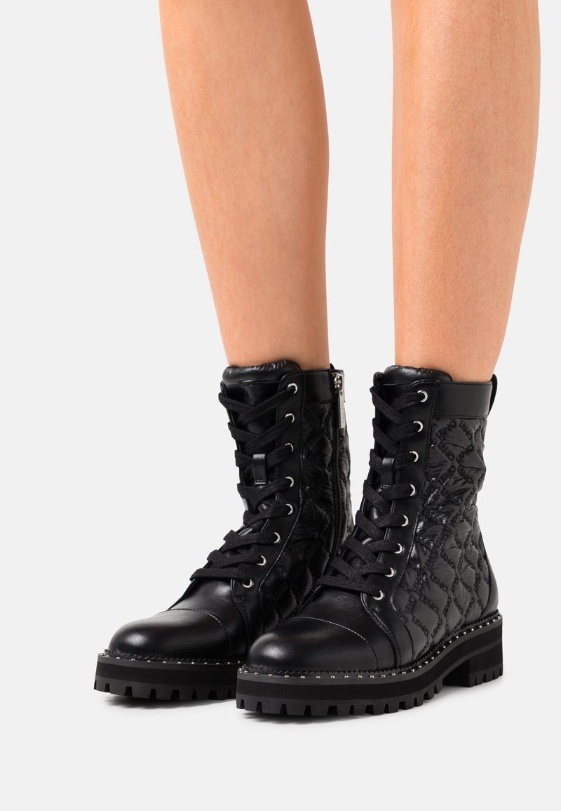 Botas de combate negras con cordones, con un acabado texturizado, que presentan una suela duradera, un patrón acolchado y ojales plateados para los cordones.