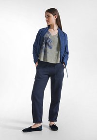 Codzienny strój z teksturowaną granatową marynarką, jasnozielonym T-shirtem z nadrukiem, ciemnymi spodniami oraz płaskimi aksamitnymi butami. Ogólnie swobodny krój.