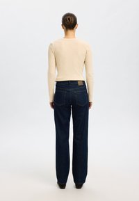 Bézs színű, hosszú ujjú, bordázott textúrájú felső, sötétkék, bő szárú farmernadrággal, melynek hátul zsebei és egy világosbarna bőr címkéje van.