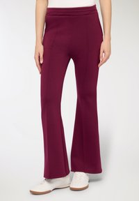 Pantaloni svasati color granato realizzati in materiale morbido, con vita alta e cuciture verticali, abbinati a sneakers bianche.