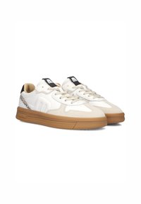 Witte en beige sneakers met een gestructureerde lichtbruine rubberen zool, complexe oppervlaktedetails en een zwart logo op de tong.