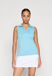 Camisola tipo polo sem mangas de cor azul clara com textura canelada e colarinho branco. Apresenta um pequeno logótipo do lado esquerdo. Usada com uma saia branca.