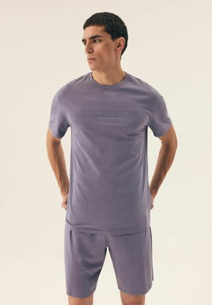 Lila Kurzarm-T-Shirt mit eingeprägtem "HENDERSON"-Text auf der Vorderseite, kombiniert mit passenden Shorts, beide aus einem glatten Stoff.