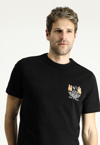 Camiseta de algodón negra de mangas cortas, con un gráfico de color claro de una furgoneta, árboles y el texto "Es hora de viajar" en el frente.