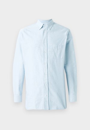 Camisa de botones de manga larga en azul claro, hecha de algodón. Cuenta con un cuello con punta y un único bolsillo en el pecho. Textura suave.