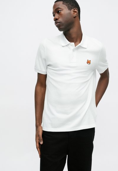 Tricou polo alb din bumbac, cu un mic broderie a unei vulpi portocalii pe pieptul stâng. Mâneci scurte și un design clasic al gulerului.