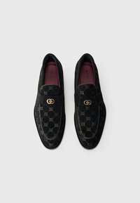 Mocassins noirs en daim doux avec une texture à motifs. Dotés d'un accent en métal doré et d'une semelle intérieure bordeaux. Design classique.
