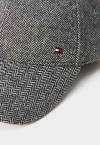 Gray houndstooth cap made of wool blend fabric, featuring a rounded shape and a small logo tag in red, white, and black on the side.