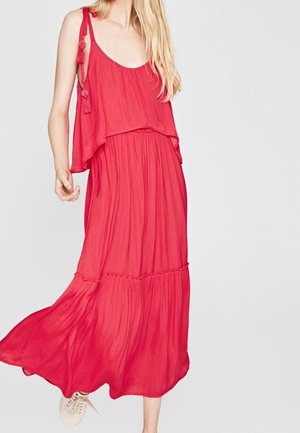 Maxi sukienka w jaskrawoczerwonym kolorze, o zwiewnym fasonie, warstwowym kroju i regulowanych ramiączkach z ozdobami w formie pomponów. Wykonana z lekkiego materiału.