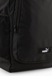 Czarny plecak wykonany z wytrzymałego materiału o teksturowanym wykończeniu, z boczną siateczkową kieszenią i wyraźnym logo Puma na prostokątnej łatce.