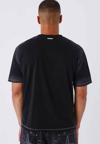 Camiseta de algodón negra con mangas cortas, corte relajado y costuras en contraste. Presenta una pequeña etiqueta en la parte posterior del cuello.