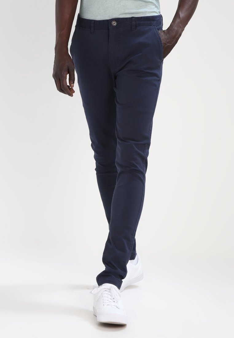 Navy blue slim-fit chinos with a button closure, featuring side pockets and a smooth cotton blend fabric. Worn with white sneakers.