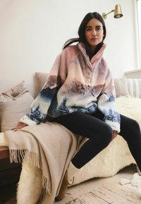 Fleece pullover with a high collar, featuring a mountain scene in pastel colors, and long sleeves. Paired with black leggings.