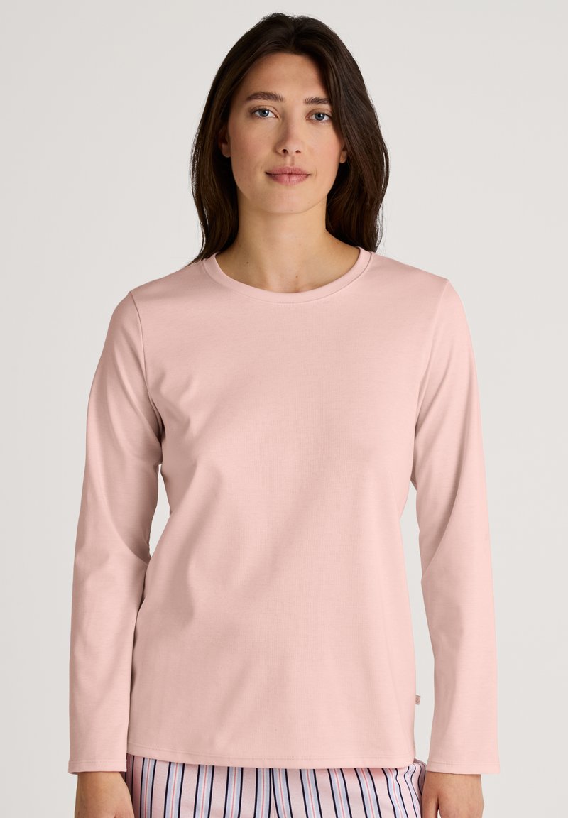 Long-sleeve, round-neck top in soft pink fabric. Features a smooth texture with minimal detailing. Paired with striped pajama bottoms.