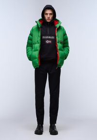 Chaqueta acolchada verde con detalles rojos, sudadera negra con un logo, pantalones negros y botas negras. Textura suave con un diseño grueso e insulated.