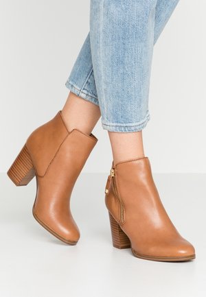 Bottes cheville en cuir marron clair avec talons blocs empilés et fermetures éclair latérales, portées avec un jean court bleu clair.