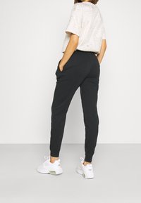 Svarta joggingsbyxor med sidofickor och ribbade muddarna, matchade med en ljusfärgad t-shirt med grafik och vita sportskor.