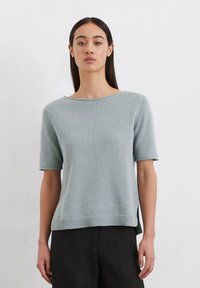 Helles, blaues Kurzarm-Pullover in einem strukturierten Strickdesign. Verfügt über einen weiten Ausschnitt und seitliche Schlitze für mehr Bewegungsfreiheit. Kombiniert mit dunkel, locker sitzenden Hosen.