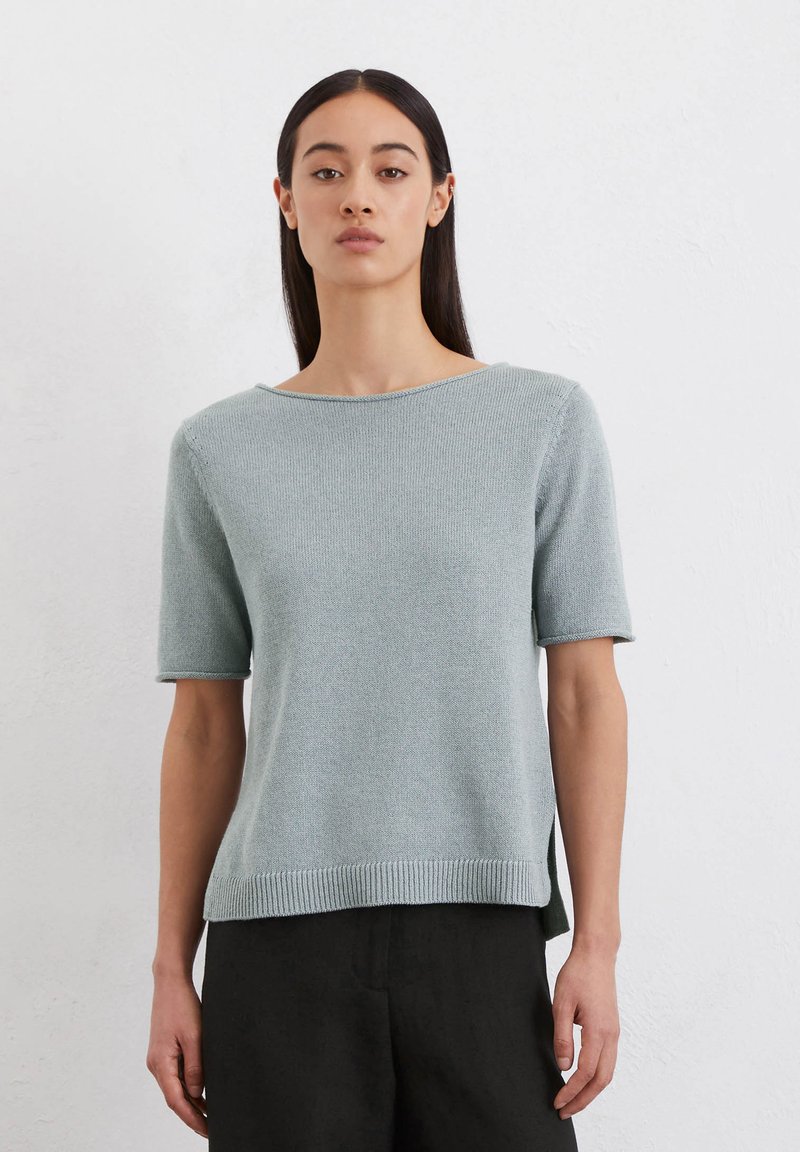Helles, blaues Kurzarm-Pullover in einem strukturierten Strickdesign. Verfügt über einen weiten Ausschnitt und seitliche Schlitze für mehr Bewegungsfreiheit. Kombiniert mit dunkel, locker sitzenden Hosen.