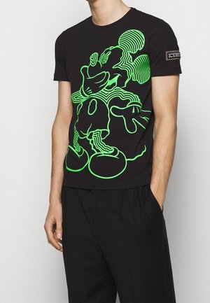 Sort bomulds t-shirt med et neongrønt grafisk motiv af en tegneseriefigur. Korte ærmer med et logo patch på venstre arm.