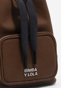 Hnedý látkový batoh s námorníckymi šnúrkami, striebornými kovovými prvkami a prednou kapsou s bielym logom "BIMBA Y LOLA".