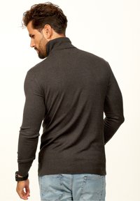 Dunkelgrauer Rollkragenpullover aus glattem Strickmaterial, mit einem gerippten Kragen und Bündchen, getragen zu hellblauen Jeans.