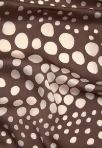 Brun stof med uregelmæssige hvide prikker i varierende størrelser, vist med bløde folder og en glat tekstur.