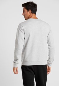 Sudadera de algodón gris con cuello redondo, puños y cintura acanalados; presenta una textura lisa, llevada sobre pantalones negros.