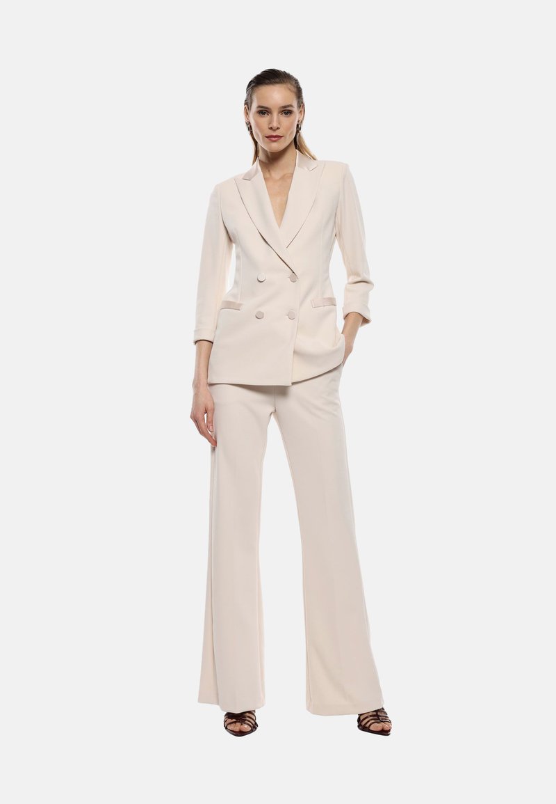 Blazer doppio petto beige chiaro con maniche a tre quarti e pantaloni svasati coordinati, caratterizzati da un tessuto liscio e dettagli minimi.