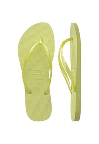 Tongs jaune clair avec semelle texturée, brides en plastique souple et logo Havaianas imprimé. Conçues pour un usage décontracté.
