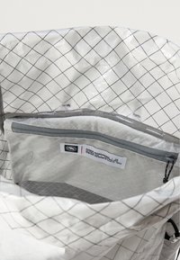 Λευκή αδιάβροχη τσάντα πλάτης με εσωτερικό σε σχέδιο πλέγματος. Διαθέτει μια γκρίζα τσέπη με φερμουάρ και ετικέτα με το λογότυπο "EIGER NORWAND". Λείος υφασμάτινος ιστός.