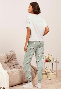 Světle šedé tričko s krátkým rukávem v kombinaci se zelenými pyžamovými kalhotami se vzorem domů v růžové a bílé barvě. Měkká tkanina s volným střihem.