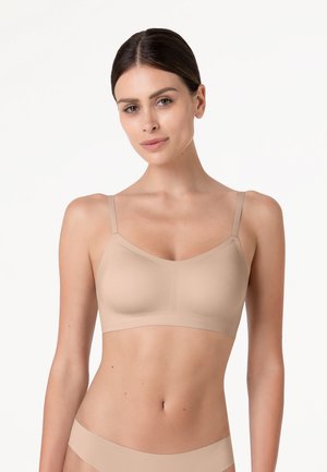 Donna con capelli scuri che indossa un reggiseno senza cuciture color nude e biancheria intima coordinata su uno sfondo bianco semplice.