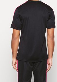 Svart tränings t-shirt med rosa accent vid axlarna och sömmarna. Tillverkad av ett slätt, lätt material, med en avslappnad passform och korta ärmar.