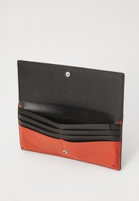 Lederbörse mit schwarzem Innenraum und kontrastierender orangefarbener Außenseite. Verfügt über mehrere Kartenfächer und einen Druckknopfverschluss. Glatte Textur.