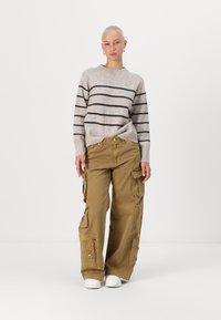 Light gray striped sweater with a crew neckline, paired with loose khaki cargo pants featuring multiple pockets and zippers. White sneakers.