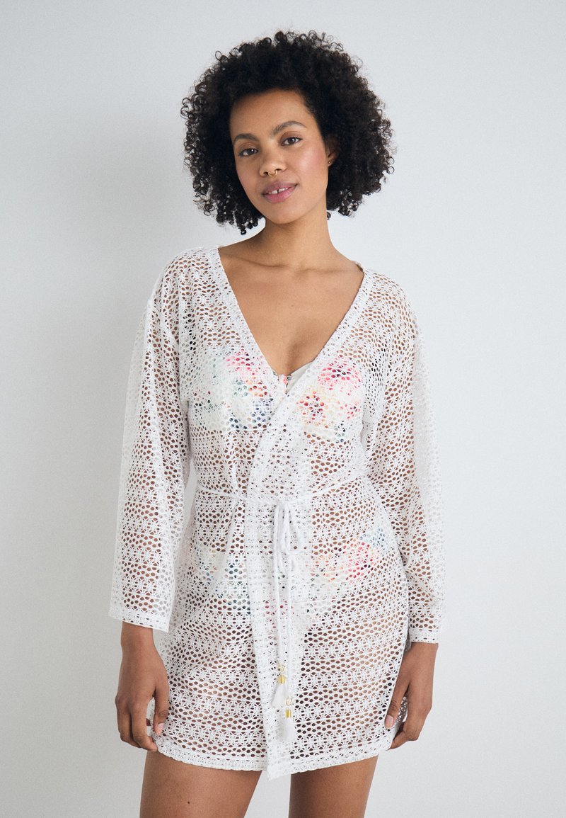 Cubierta de encaje blanca con diseño de escote en V, mangas largas, cintura con cordón y un colorido patrón floral debajo. Textura ligera y transpirable.