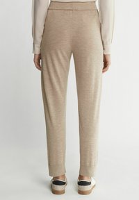 Beige tapered Jogginghosen mit feiner Textur, elastischem Bund und gerippten Bündchen. Getragen mit lässigen Sneakers mit kontrastierendem schwarzen Akzent.