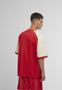 Punainen ja beige t-paita, jossa on raglan-muotoilu, lyhyet hihat ja rento malli. Sujuva rakenne ja kontrastivärit hihoissa.