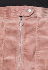 Jupe en velours côtelé rose avec des côtes verticales, dotée d'une fermeture éclair argentée et d'un bouton-pression à la taille. Texture lisse, design mi-long.