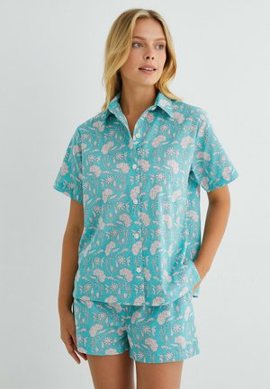 Ensemble en turquoise composé d'une chemise à manches courtes et d'un short avec un motif floral blanc. Comprend un col, une fermeture à boutons et des poches latérales.